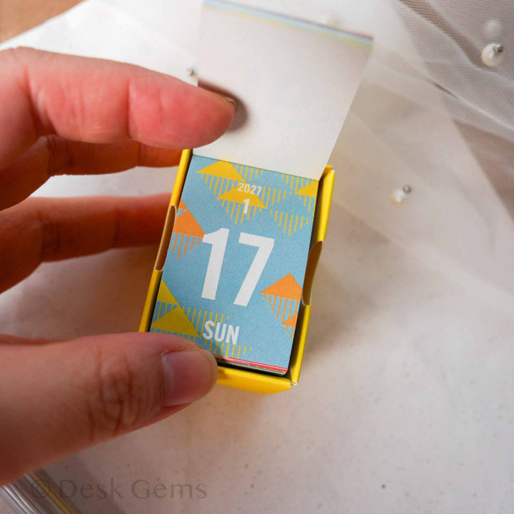 Shinnippon Mini Mini Daily Calendar 2027 Dates open showing January 17 page with blue and yellow triangle pattern