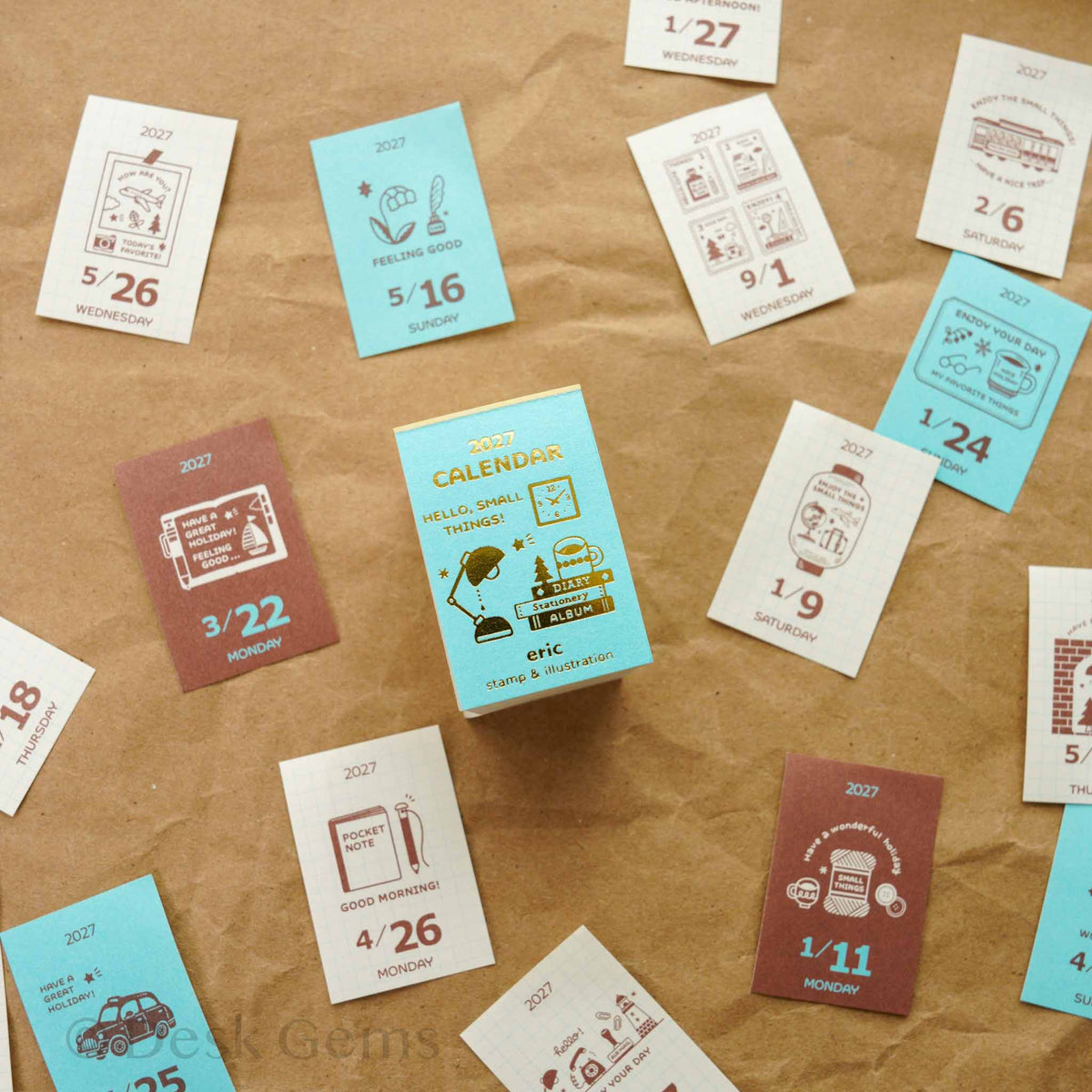 Eric Small Things Mini Mini Daily Calendar 2027 teal box with scattered daily pages showing colorful stamp illustrations