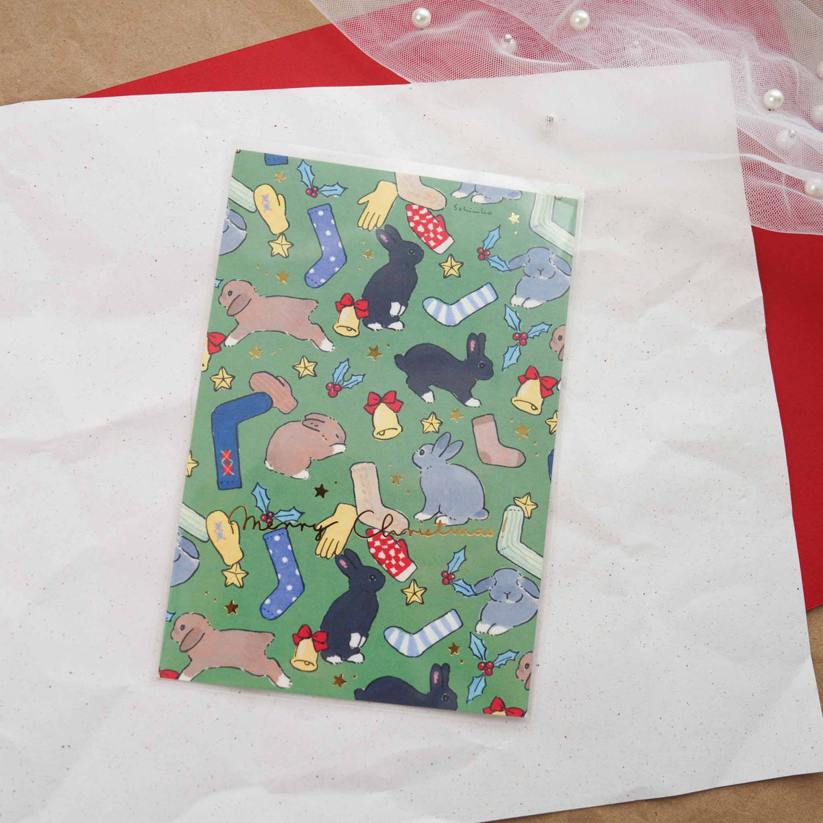 Schinako Moriyama Christmas postcard with bunnies, stockings, and mittens pattern on green background