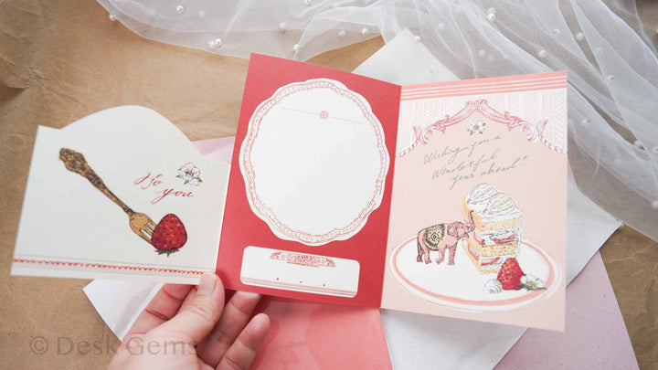 Aya Inoue trifold birthday card fully opened showing three panels: strawberry fork, writing space, and elephant with cake illustration